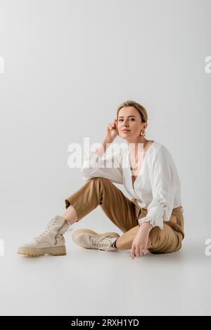 Attraktive blonde Frau in lässiger Business-Pastellkleidung auf dem Boden sitzend, stilvoll und modisch Stockfoto