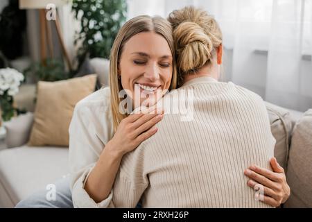 Niedliche, attraktive Schwestern in trendigen Pastelloutfits, die sich aufrichtig umarmen und lächeln, Familienbindung Stockfoto