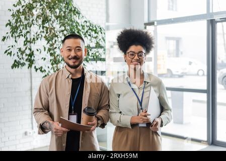 Professionelle Headshots, zwei verschiedene Büroangestellte mit Laptop, Ordner und Kaffee für unterwegs im Büro Stockfoto