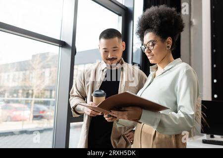 afroamerikanische Frau zeigt Startup-Projekt im Ordner für asiatischen Geschäftsmann in Coworking Stockfoto