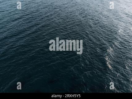 Bild einer ruhigen und friedlichen blauen Meeresoberfläche mit kleinen Wellen. Dunkles und stimmungsvolles Wasser im Ozean während des Sonnenuntergangs. Foto von Wellen im Meer oder Ozean Stockfoto