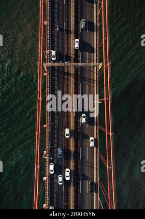 Vertikales Foto des Verkehrs auf der Brücke, die den Fluss überquert - Draufsicht. Brücke in Lissabon (Portugal) mit Autos und anderen Fahrzeugen von oben (Luftaufnahme). Stockfoto