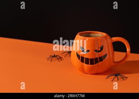 Cappuccino Latte Kaffee in Kürbisbecher auf schwarzem orangefarbenem Hintergrund. Halloween-Feier-Konzept Stockfoto