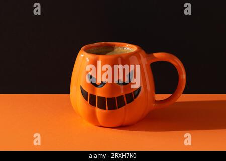 Cappuccino Latte Kaffee in Kürbisbecher auf schwarzem orangefarbenem Hintergrund. Halloween-Feier-Konzept Stockfoto