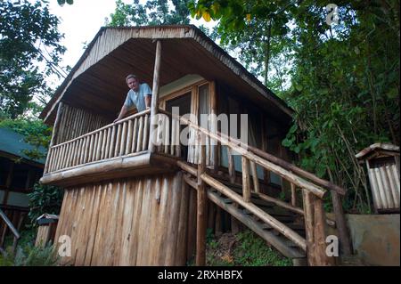 Der Mann steht auf der Veranda seiner Hütte mit Blick auf die Kamera, in der Nähe des Bwindi Inpenetrable Forest National Park in Uganda; Uganda Stockfoto