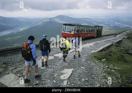 Der Zug ist voller Touristen und fährt an Wanderern vorbei, die den Mount Snowdon in Wales, Wales, hinabsteigen Stockfoto