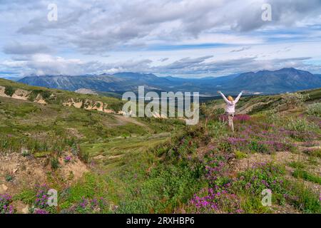 Rückansicht einer Person auf dem Montana Mountain mit erhobenen Händen beim Blick auf die wunderschöne aussicht in der Nähe von Carcross, Yukon Territory Stockfoto