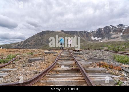 Rückansicht von zwei Personen, die auf einer alten Bergbaubahn stehen, während sie sich mit den Hügeln des Montana Mountain in der Nähe von Carcross, Yuko teilt... Stockfoto