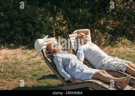 Ein paar süße ältere Leute liegen auf den Liegen und halten die Hände in der Sonne. Stockfoto