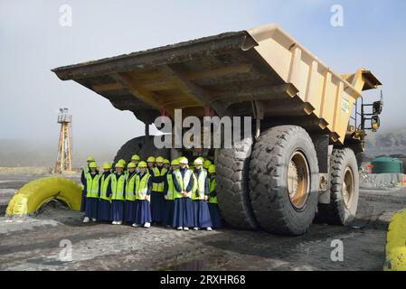 WESTPORT, NEUSEELAND, 31. AUGUST 2013: Schulmädchen auf einer Klassenexkursion posieren am 31. August 2013 unter einem riesigen Truck in einer offenen Kohlengrube Stockfoto