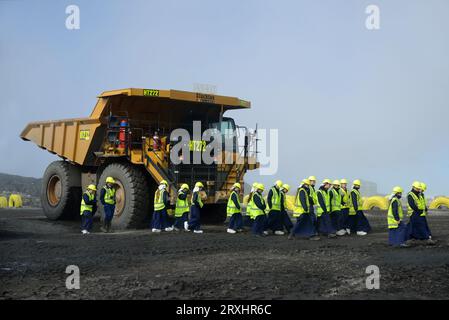 WESTPORT, NEUSEELAND, 31. AUGUST 2013: Schulmädchen auf einem Klassenausflug spazieren am 31. August 2013 an einem riesigen Truck in einer offenen Kohlengrube vorbei Stockfoto