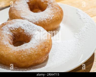 Süße leckere Donuts, bestreut mit Puderzucker auf dem weißen Teller auf dem hölzernen Hintergrund Stockfoto