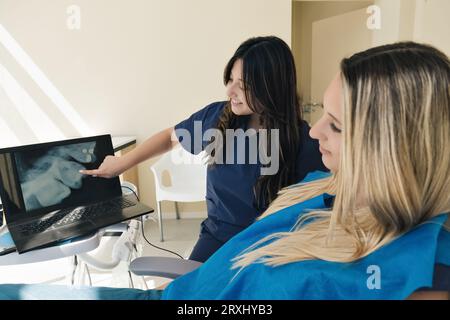 Zahnärztin zeigt dem Patienten die Röntgenaufnahme auf dem Laptop. Ein Zahnarzt, der eine Röntgenaufnahme mittels Technik zeigt. Stockfoto