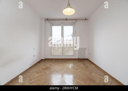 Kleines leeres Wohnzimmer mit weißem Aluminiumfenster und lackiertem Glas, Aluminiumkühler und Parkettboden aus Eiche mit Fischgrätmuster Stockfoto