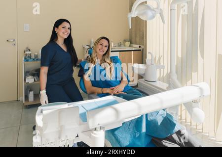 Schöne junge Patientin im Zahnarztstuhl sitzend. Patient und Zahnarzt schauen und lächeln in die Kamera. Stockfoto
