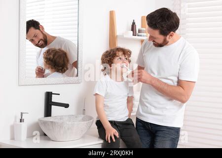 Vater hilft seinem Sohn, im Bad Zähne zu putzen Stockfoto