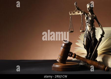Statue von Lady Justice in der Nähe von Gavel und offenem Buch auf dunklem Tisch, Platz für Text. Symbol der gerechten Behandlung nach dem Gesetz Stockfoto