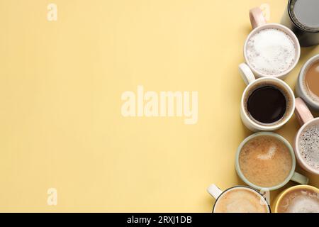 Viele verschiedene Tassen mit aromatischem Kaffee auf gelbem Tisch, flach liegend. Leerzeichen für Text Stockfoto