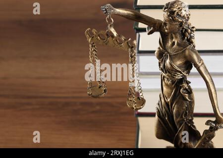 Symbol der gerechten Behandlung nach dem Gesetz. Figur der Lady Justice und Bücher auf Holztisch, Nahaufnahme mit Platz für Text Stockfoto