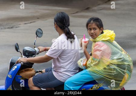 SAMUT PRAKAN, THAILAND, Juni 2023, Eine Frau reitet ein Motorrad mit einem Mädchen in einem Regenmantel Stockfoto