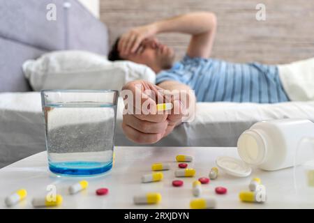 Junger Mann, der Medizin-Pille für Kater im Bett zu Hause nimmt, leidet an Kopfschmerzen, Migräne. Ein Mann leidet unter Kopfschmerzen während einer Erkältung während des Liegens Stockfoto