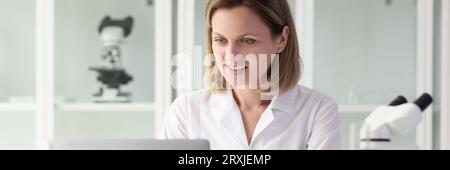 Zufriedene Forscherin, die am Labortisch am Laptop arbeitet. Stockfoto