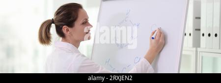 Glückliche Wissenschaftlerin, die chemische Formeln auf dem Whiteboard zeichnet. Stockfoto