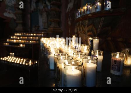 Beleuchtete Votivkerzen in der San Xavier del Bac Mission in der Nähe von Tucson, Arizona. Einige der geschnitzten und bemalten Dekorationen der Mission sind dahinter zu sehen Stockfoto