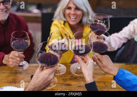 Bei einer Nahaufnahme werden sechs Weingläser auf einer Außenterrasse getoastet, die die Eleganz des Weins und den geselligen Geist der gemeinsamen Momente unterstreichen Stockfoto