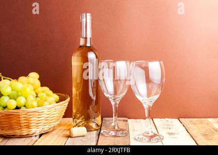 Von oben aus Gläser und eine Flasche Wein mit frischen Traubenfrüchten im Korb auf einem Holztisch im Zimmer mit braunem Hintergrund in Tageslicht Stockfoto