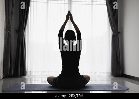 Eine asiatische Frau, die im Haus auf einer Yogamatte Yoga praktiziert, übt Meditation, um sich zu entspannen. Ideen für Heimübungen. Stockfoto
