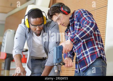 Mann, der den Mentor beim Bohren eines Holzbretts beobachtet Stockfoto