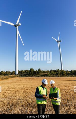 Ingenieure, die mit einem Laptop auf einem Feld von Windmühlen arbeiten Stockfoto