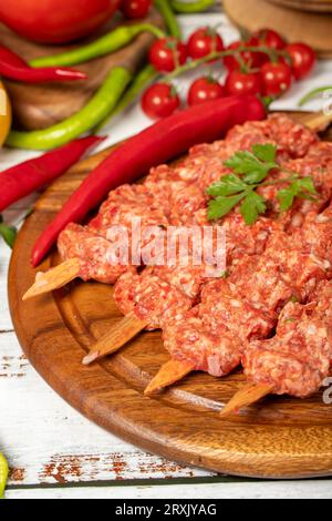 Adana Kebab auf Holzgrund. Roher Shish adana Kebab mit Kräutern und Gewürzen. Nahaufnahme Stockfoto