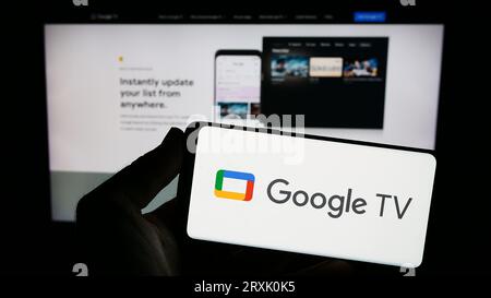 Person, die ein Smartphone mit dem Logo des Video-on-Demand-Dienstes Google TV auf dem Bildschirm vor der Website hält. Konzentrieren Sie sich auf das Display des Telefons. Stockfoto
