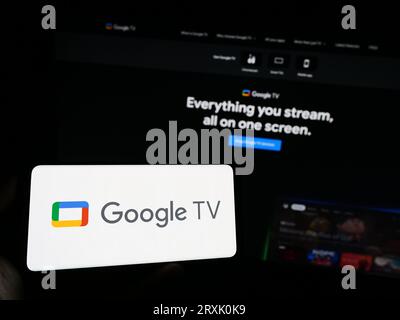Person, die ein Mobiltelefon mit dem Logo des Video-on-Demand-Dienstes Google TV auf dem Bildschirm vor der Geschäftswebseite hält. Konzentrieren Sie sich auf das Display des Telefons. Stockfoto