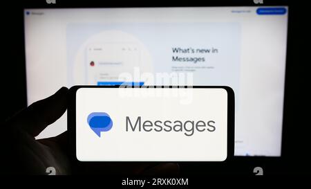 Person, die ein Smartphone mit dem Logo der Instant Messaging-App „Google Messages“ auf dem Bildschirm vor der Website hält. Konzentrieren Sie sich auf das Display des Telefons. Stockfoto