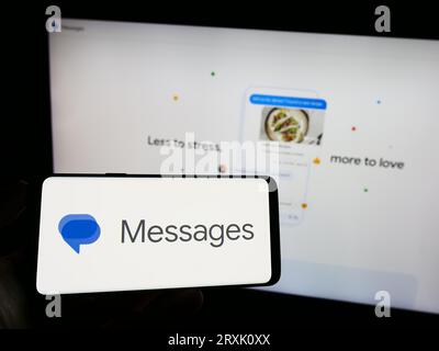 Person, die ein Mobiltelefon mit dem Logo der Instant Messaging-App „Google Messages“ auf dem Bildschirm vor der geschäftlichen Webseite hält. Konzentrieren Sie sich auf das Display des Telefons. Stockfoto