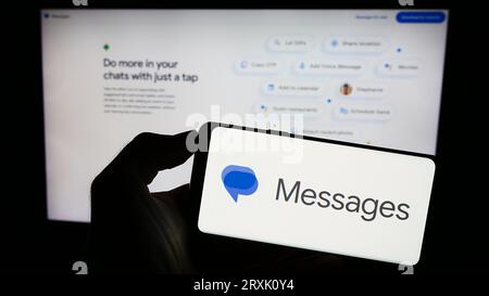 Person, die ein Mobiltelefon mit dem Logo der Instant Messaging-App „Google Messages“ auf dem Bildschirm vor der Unternehmenswebsite hält. Konzentrieren Sie sich auf das Display des Telefons. Stockfoto