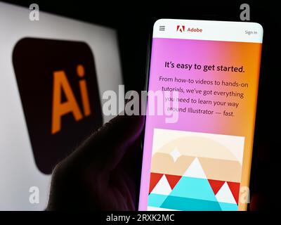 Person, die ein Mobiltelefon mit einer Webseite des Vektorgrafik-Editors Adobe Illustrator auf dem Bildschirm vor dem Logo hält. Konzentrieren Sie sich auf die Mitte der Telefonanzeige. Stockfoto