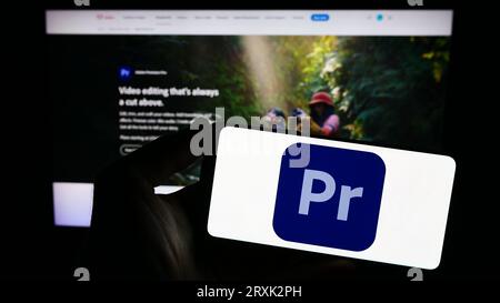 Person, die ein Smartphone mit dem Logo der Videobearbeitungssoftware Adobe Premiere Pro auf dem Bildschirm vor der Website hält. Konzentrieren Sie sich auf das Display des Telefons. Stockfoto