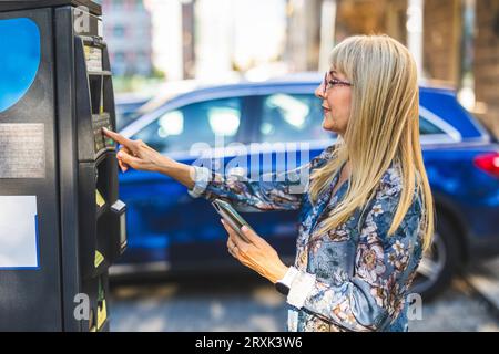 Reife Frau, die ein Handy benutzt, um für Parken in der Stadt zu bezahlen Stockfoto