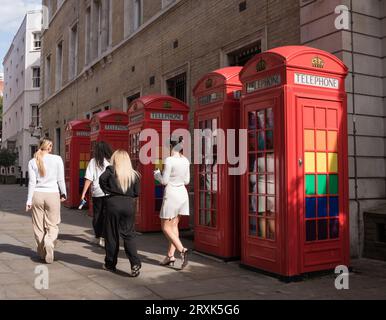 Eine Gruppe junger Frauen besteht an klassischen K6-Telefonboxen, die mit LGBTQ-Regenbogenfarben dekoriert sind, in Broad Court, Covent Garden, London, England, Großbritannien Stockfoto