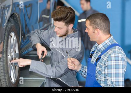 Professioneller Kfz-Mechaniker-Auszubildender, der das Autorad mit einem Schraubenschlüssel wechselt Stockfoto