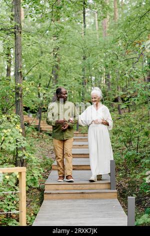 Vertikales Bild eines multiethnischen Seniorenpaares, das gemeinsam im Wald spaziert Stockfoto