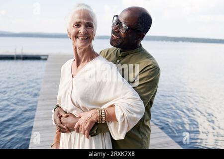 Afroamerikaner, der seine glückliche Frau umarmt, während sie auf dem Pier stehen Stockfoto