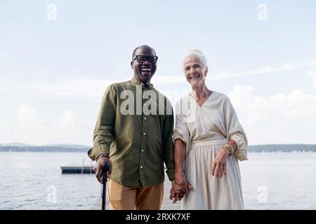 Porträt eines multiethnischen glücklichen älteren Paares, das Hände hält und vor der Kamera lächelt, während es draußen steht Stockfoto