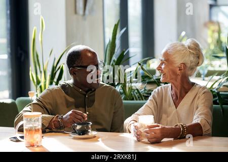 Glückliches Seniorenpaar, das Kaffee trinkt und sich mit anderen unterhält, während es im Café ausgeht Stockfoto