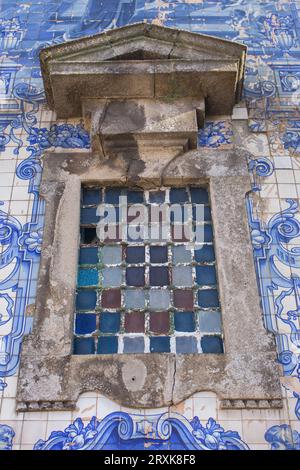 Buntglasfenster und Azulejo-Fliesen an der Kirchenfassade in Porto, Portugal. Traditionelle portugiesische Außendekoration. Alte Kirchendekoration. Stockfoto