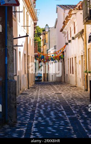 Festliche Straßendekoration in Lissabon, Polrugal. Enge mittelalterliche Straße mit Blumenkränzen und Fahnen. Siesta-Konzept. Typisch alte Straße in Europa. Stockfoto